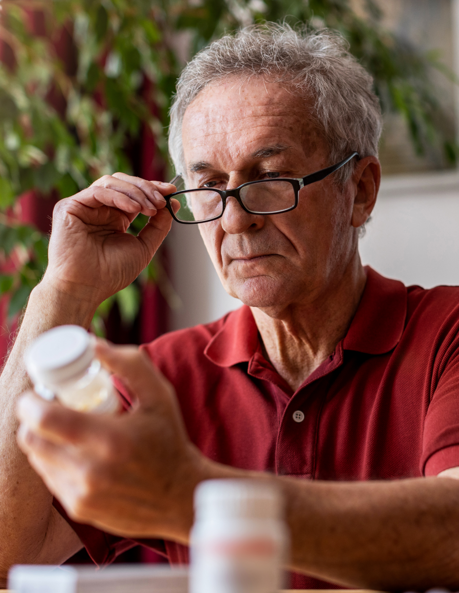 Mann liest Rückseite einer Medikamentenschachtel.